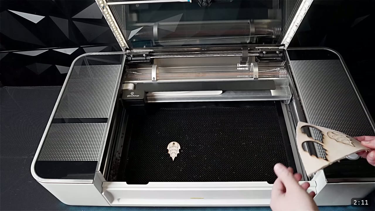 a small laser-cut leather helmet piece on the honeycomb bed of a Glowforge cutter with a hand lifting a cut chevron piece