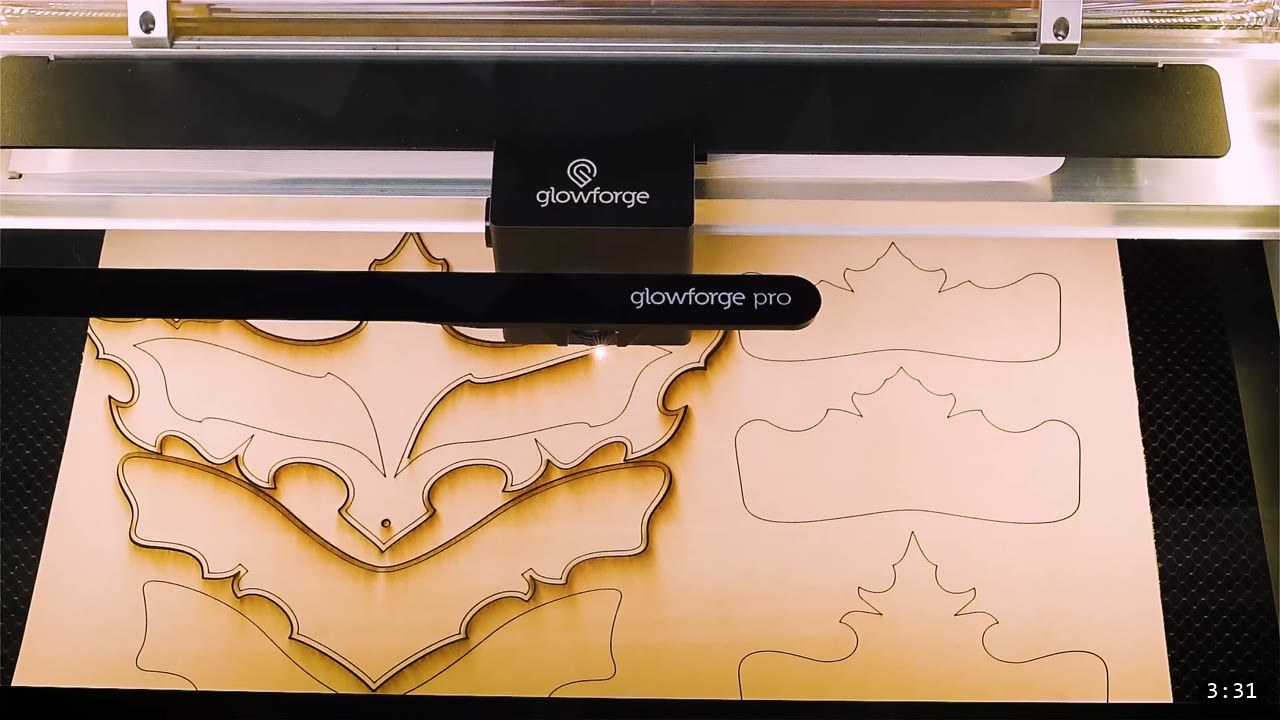 a Glowforge Pro laser head passing over a tan leather sheet, cutting intricate helmet panel shapes with scorched cut lines