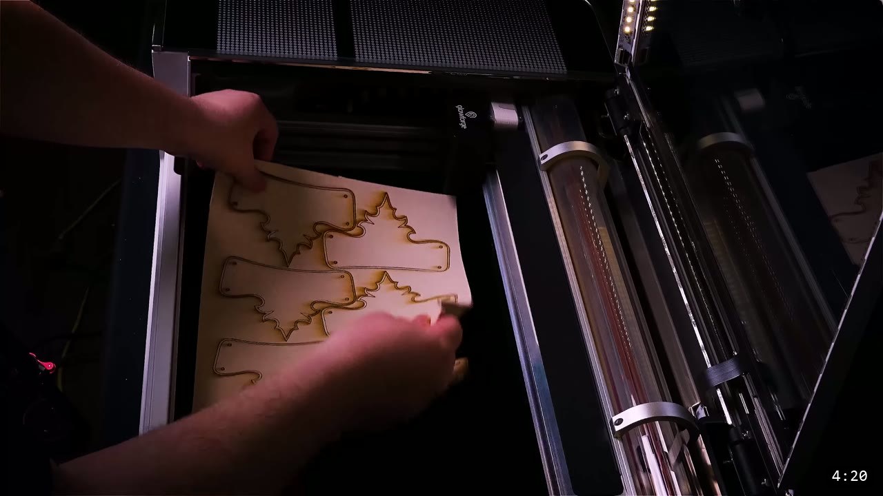 hands lifting a laser-cut leather sheet with several helmet panel shapes out of the Glowforge cutter