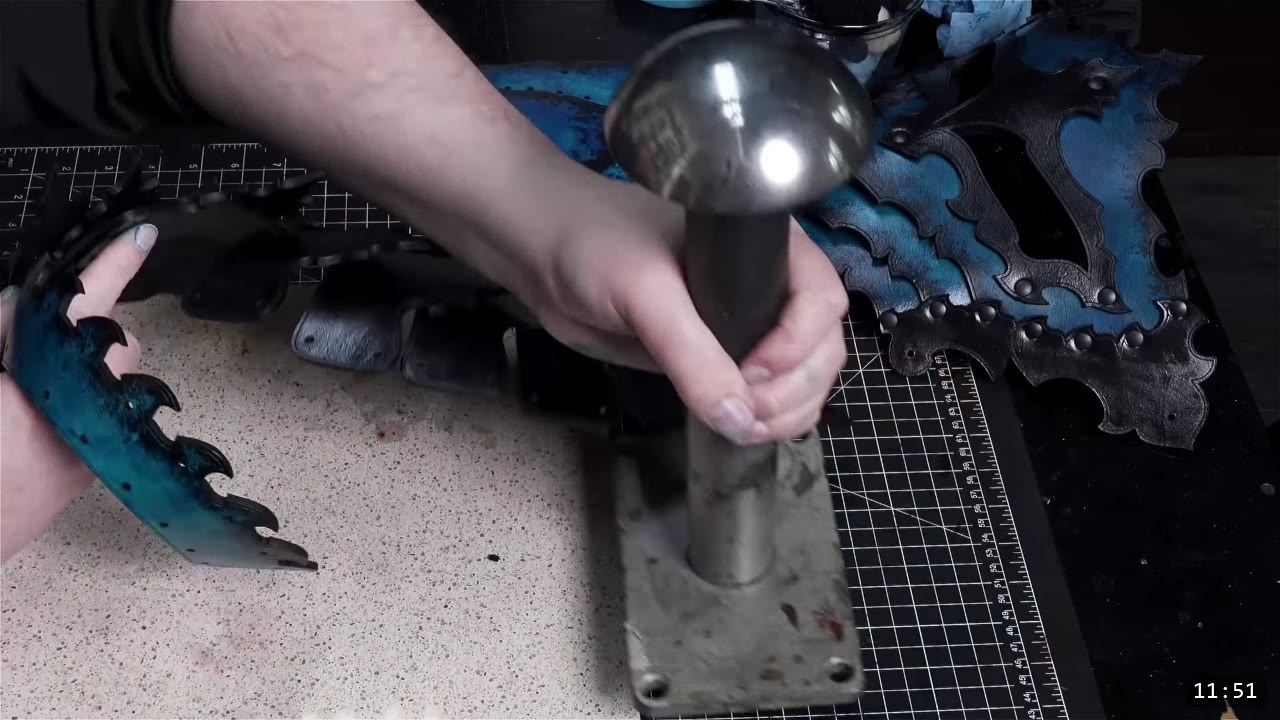 a hand setting rivets on a leather core piece over a domed metal forming stake, with a riveted dark-dyed assembly beside it
