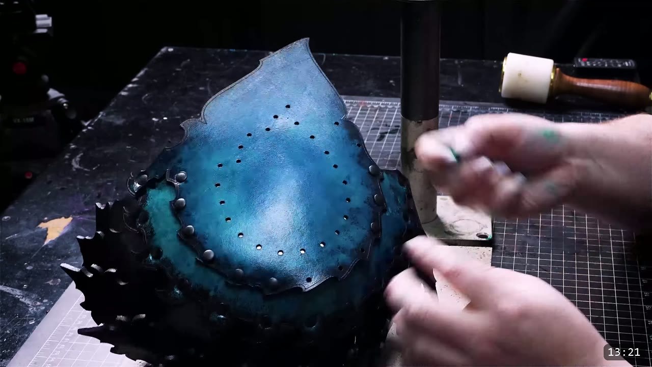 a dark blue-black leather helmet core dome, riveted along its edges, held over a granite slab while a side panel is added