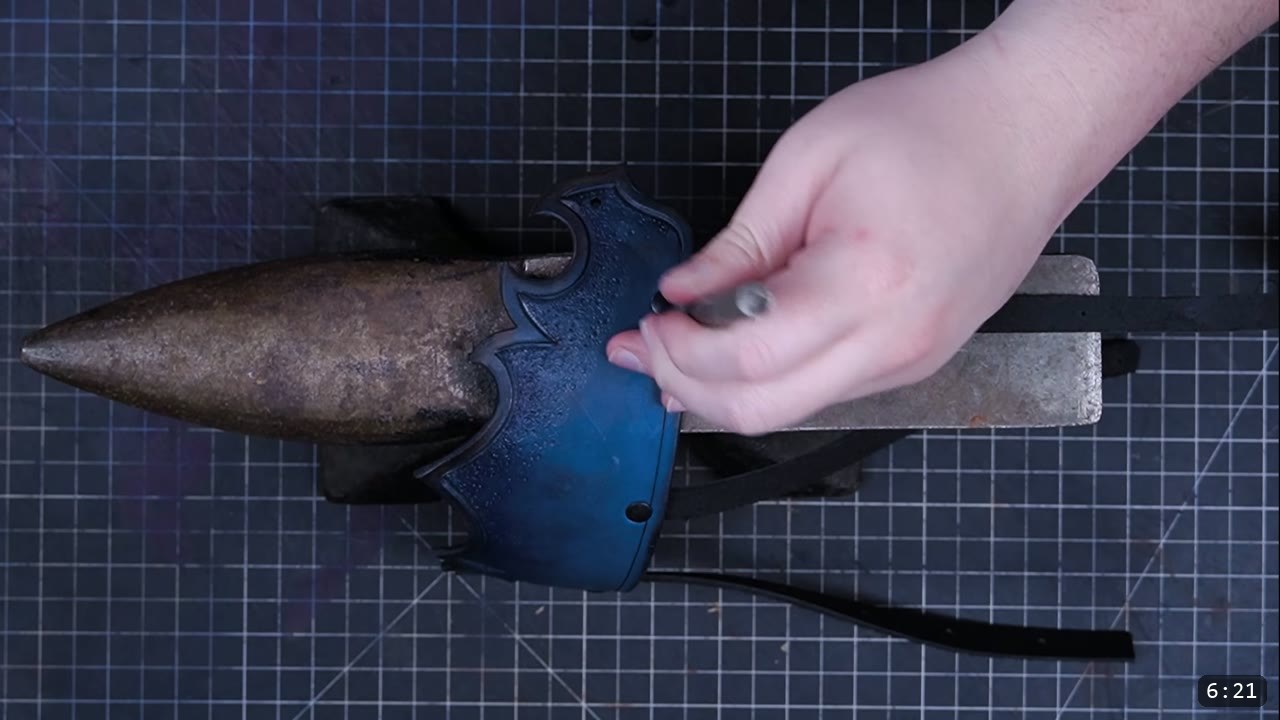 setting a rivet on the assembled blue-black pauldron over a horn anvil, a loose strap hanging below