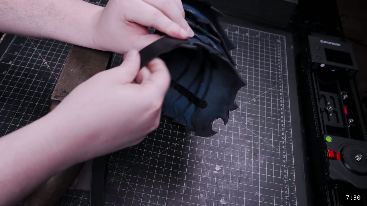 threading a black retaining strap through the back of the assembled dark pauldron on the cutting mat