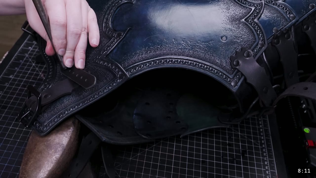 fitting a buckled strap to the finished blue-black Imperial pauldron, tooled beaded border and rivets visible, rows of punched holes on the inside face below