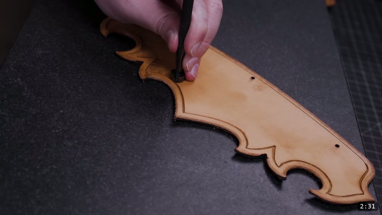 carving along the border line of a tan pauldron lame with a swivel knife on a stone slab, a beveled border groove and two punched holes visible
