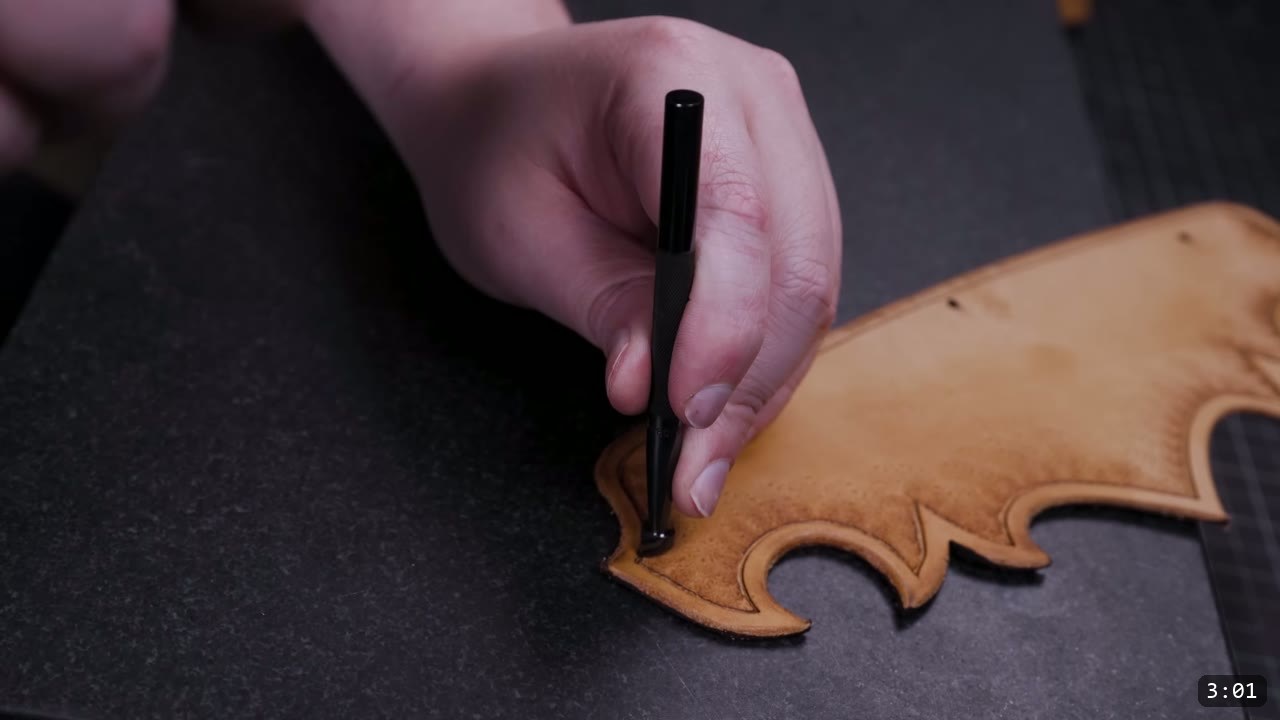 pressing a textured stamp tool along the beveled border of a tan pauldron lame on a stone slab