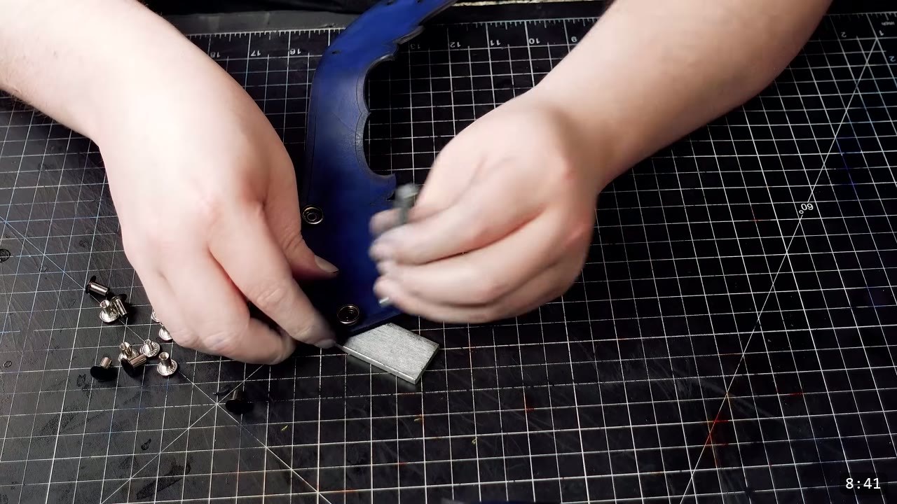 setting a metal snap on the blue sabaton with a snap setter and a steel setting block, Chicago screws scattered nearby