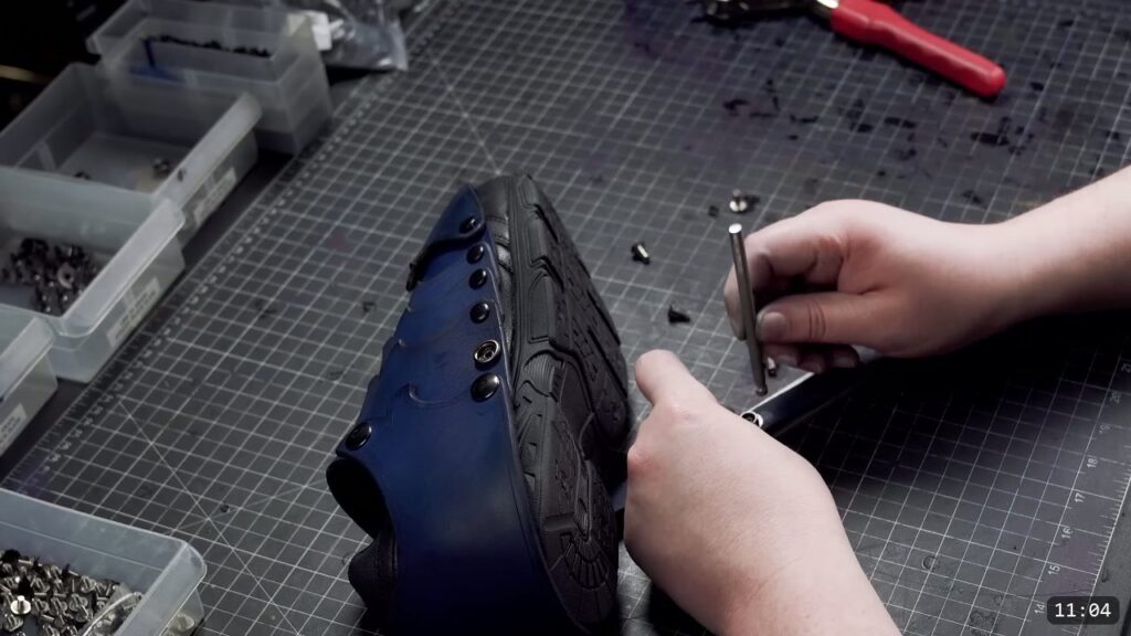 setting a fastener along the arch of the blue sabaton with a setter and a metal bar, hardware bins around the mat