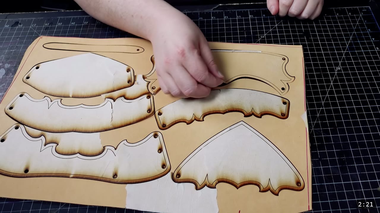 laser-cut sabaton plates with scorched edges still held in the natural leather sheet, a hand peeling one piece free