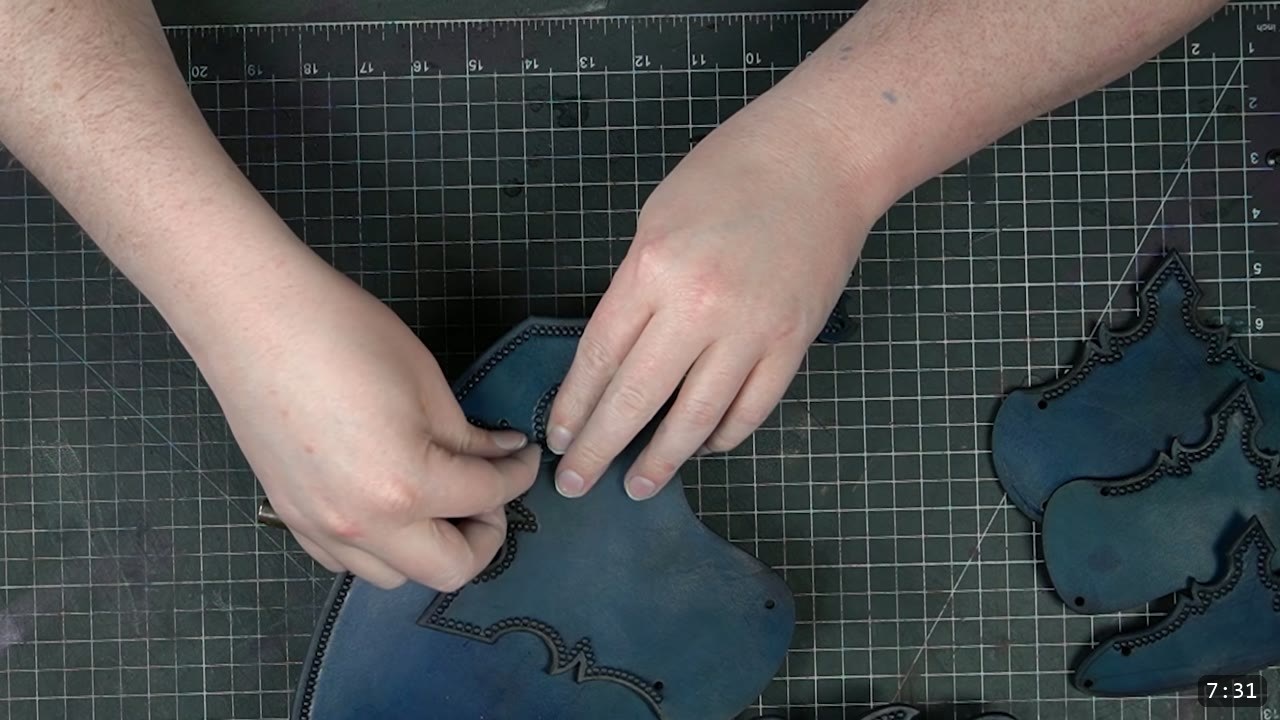 Imperial Knight Tassets Build Guide: Leather Hip Armor from a Flat Pattern 10 hands aligning two deep-blue tooled tasset plates on a grid cutting mat, a third plate resting to the side