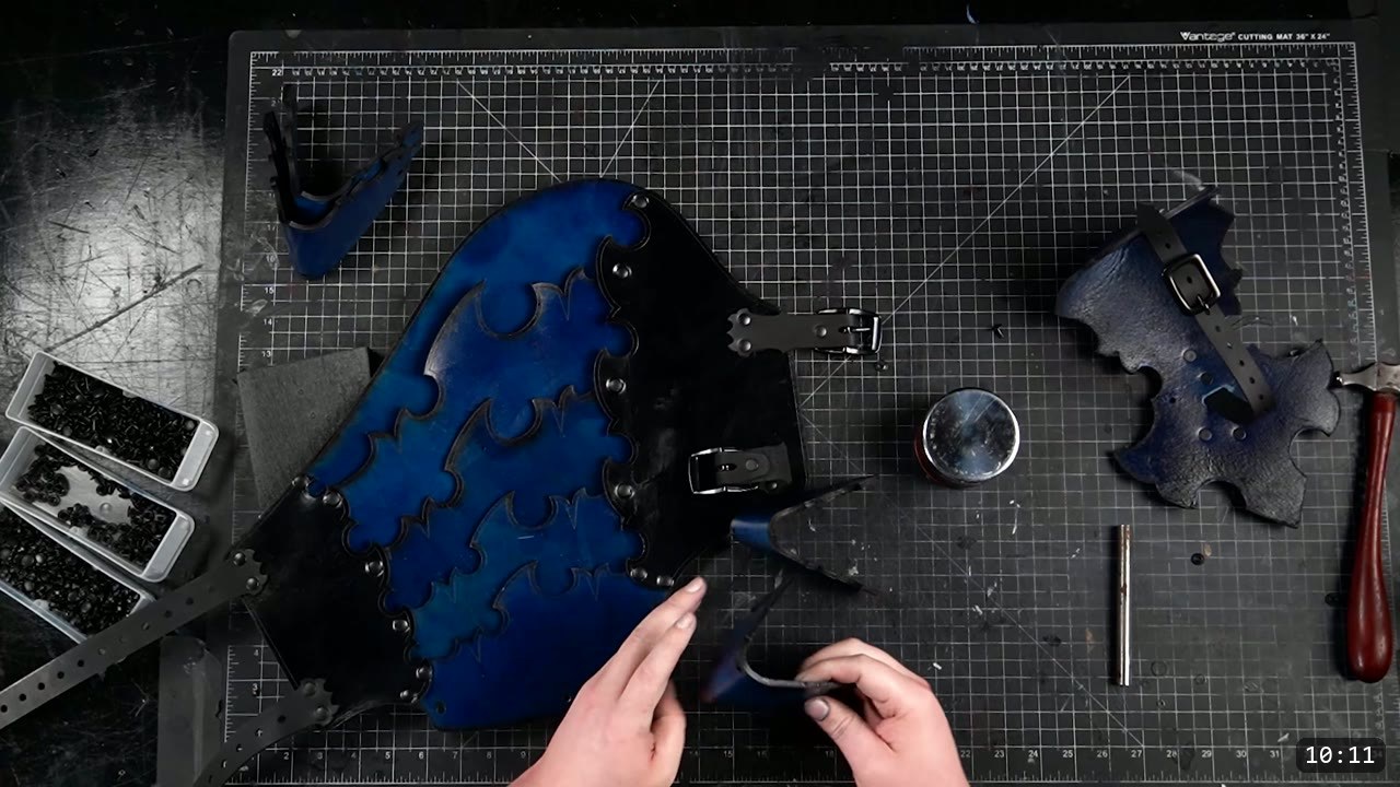 Leather Leg Armor Build Guide: Articulated Cuisses, Knees, and Greaves 11 a royal-blue cuisse on the bench with two black buckle straps riveted along one edge, rivet bins and a burnishing tin nearby