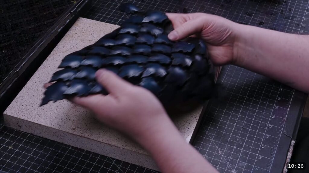 both hands holding the finished triangular royal-blue scale skirt panel of overlapping domed scales on a stone slab