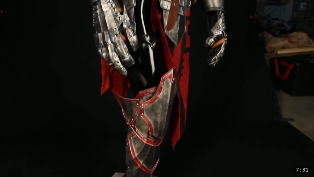 a finished red and silver leather knight armor with gauntlets and thigh plates standing on a display
