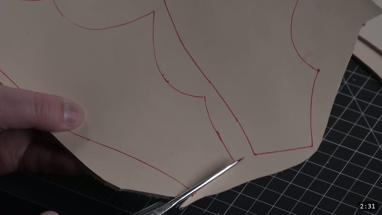 Leather Armor for Beginners: Tools You Need and How to Start 5 cutting a leather piece marked with red pattern lines using leather shears on a black cutting mat
