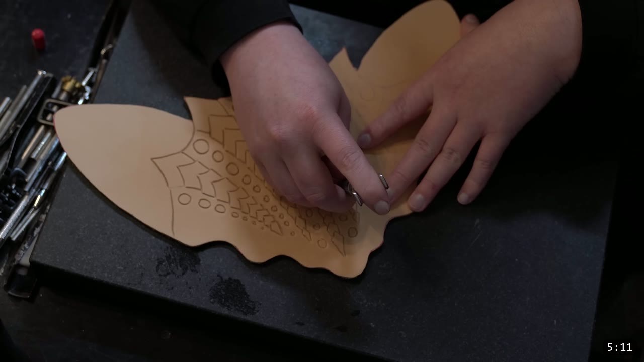 Leather Armor for Beginners: Tools You Need and How to Start 9 tooling a repeating geometric decorative pattern into a tan leather piece on a black granite slab, with hand tools laid out at the left
