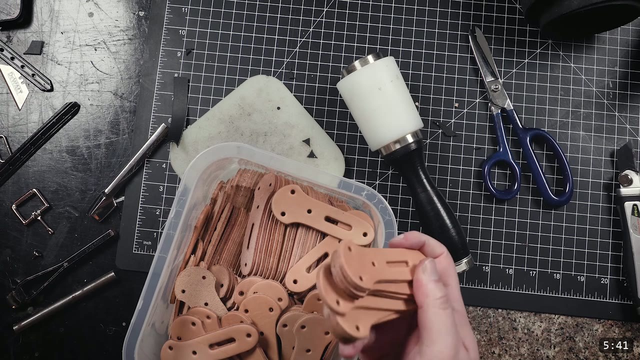 Leather Buckle Straps for Armor: A Reusable How-To with Free Patterns 12 a bin full of identical tan leather buckle strap tabs cut in bulk, with a maul and shears on the bench