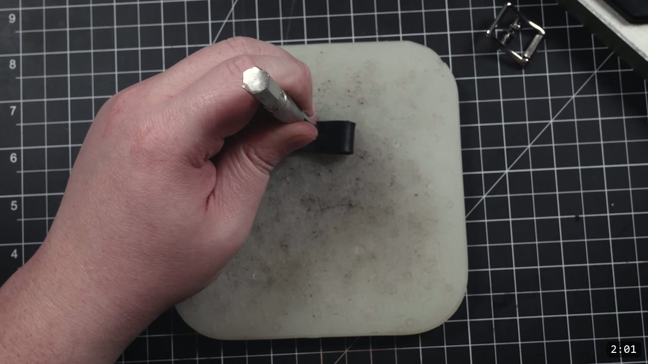 Leather Buckle Straps for Armor: A Reusable How-To with Free Patterns 5 driving a round hole punch through a folded black leather strap end on a white poly cutting board