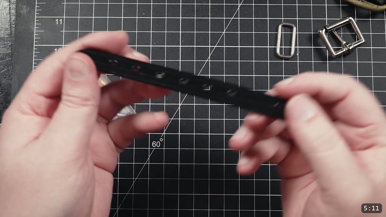 Leather Buckle Straps for Armor: A Reusable How-To with Free Patterns 9 holding a finished black strap with a row of oblong adjustment slots, a keeper loop and roller buckle on the mat