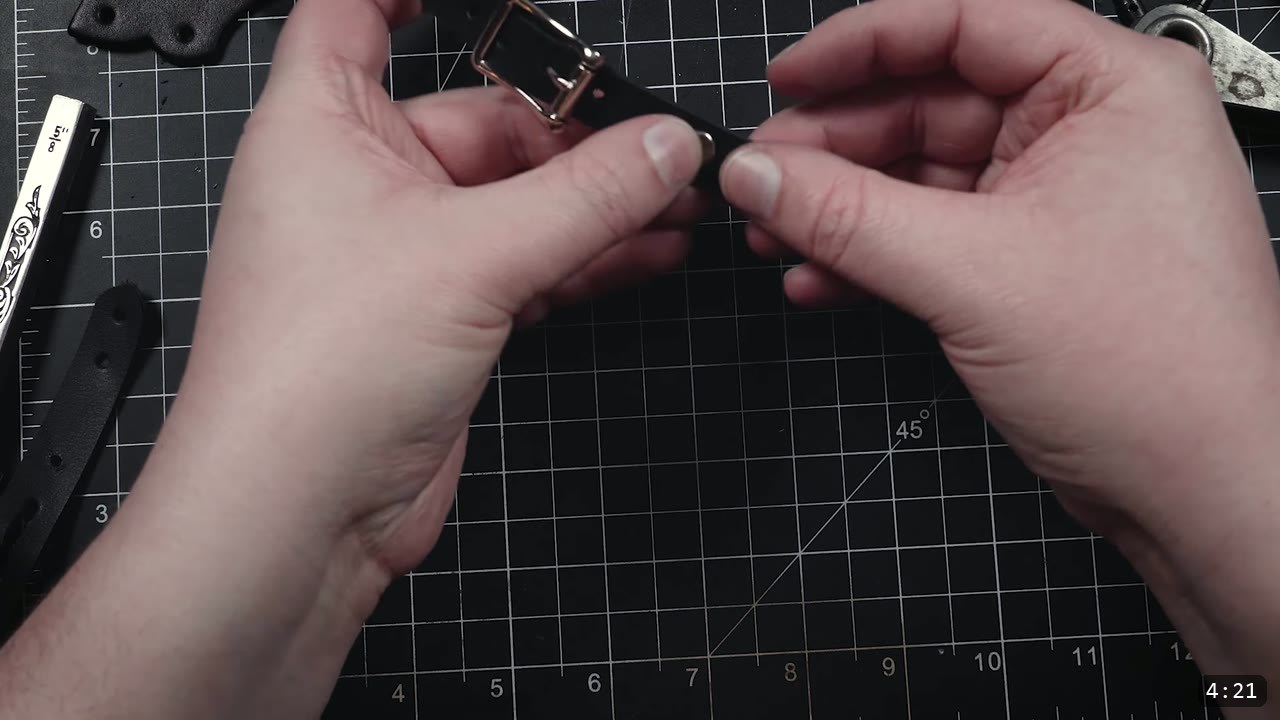Leather Buckle Straps for Armor: A Reusable How-To with Free Patterns 10 holding a completed black leather buckle strap with a set buckle and a row of punched adjustment holes