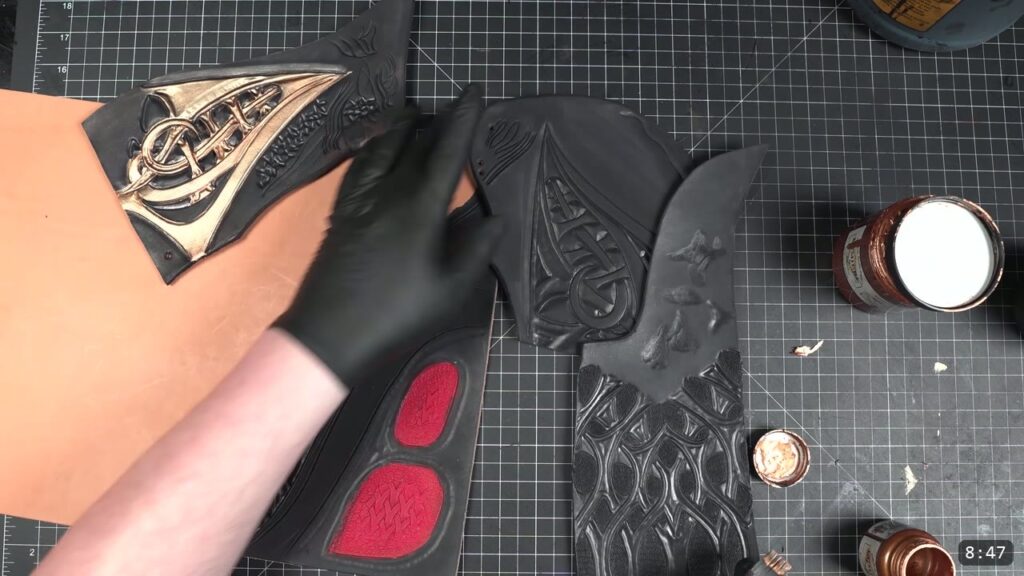a tooled sample finished in the black, red, and bronze scheme, bronze picked out on the raised filigree and red in the textured pockets, with jars of bronze metallic nearby
