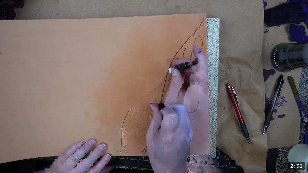 Custom Leather Armor: How I Design, Tool, and Color Test a Suit (Manticore Build) 5 hands carving and tooling the design into the tan leather sample on a stone slab, with pens and a cutting mat alongside