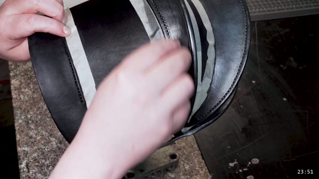 masking tape around the trim bands of the dyed-black helmet with metallic paint being blotted over the trim
