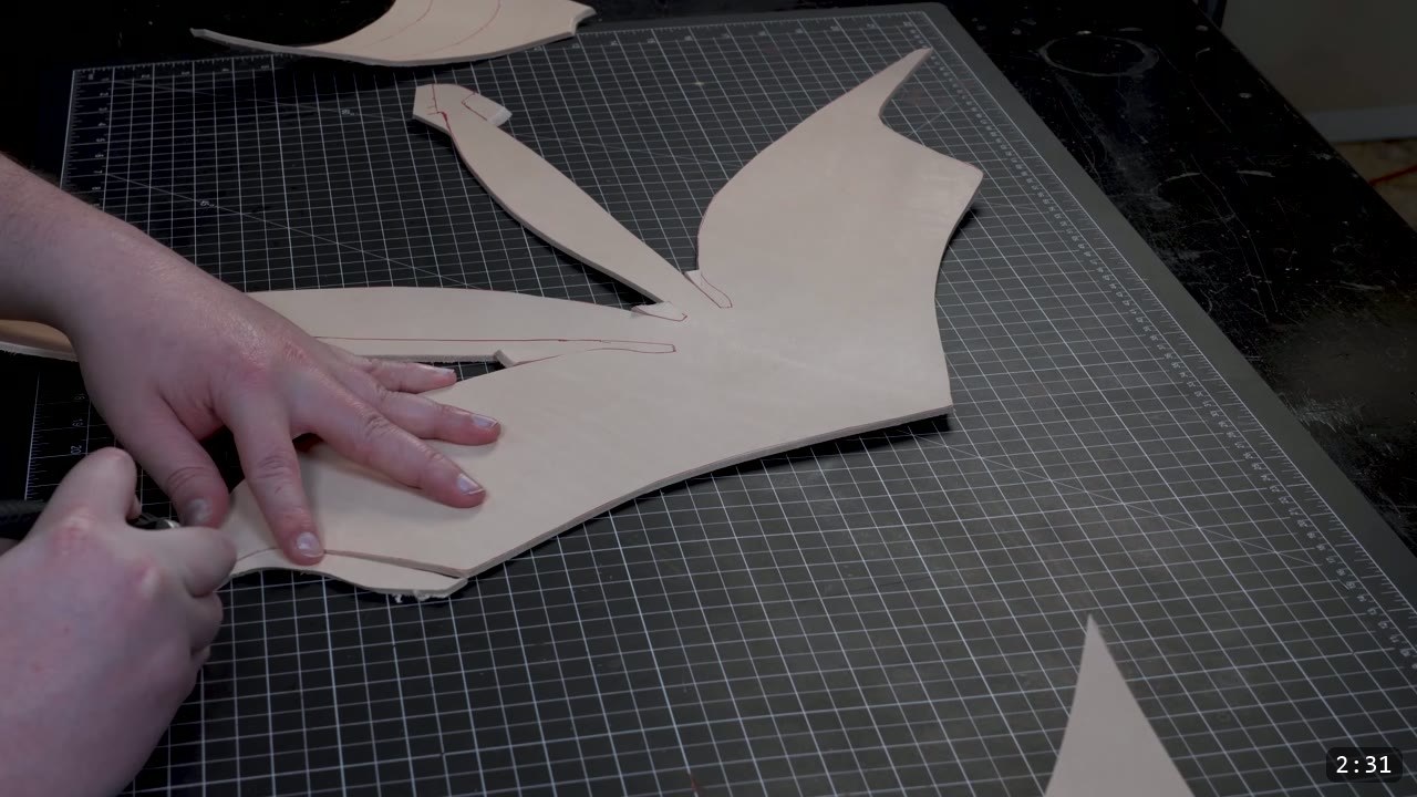The Mountain Leather Helmet Build Guide: A Free Pattern, Start to Finish 3 cut vegetable-tan helmet pieces with red traced guidelines on a cutting mat, one being trimmed with leather shears