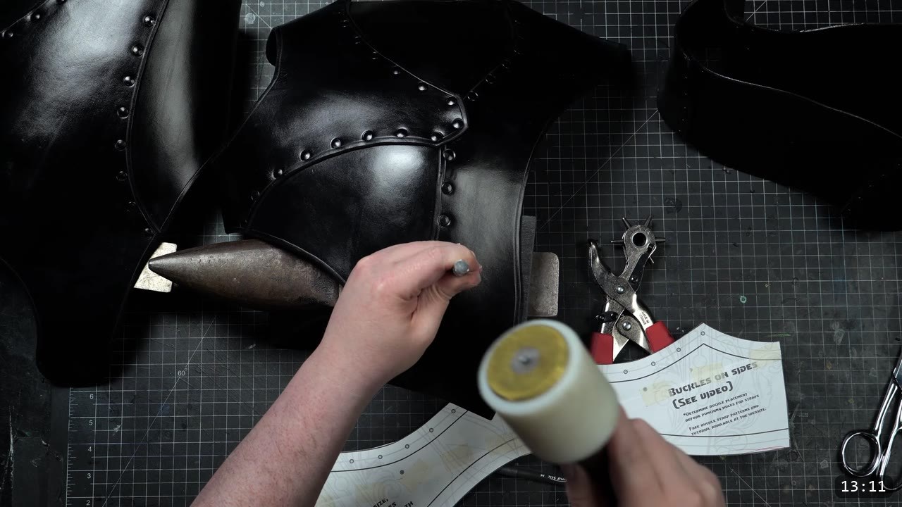setting a rivet with a setter and mallet on the dyed black plates, buckle strap pattern pieces and a rotary punch on the bench