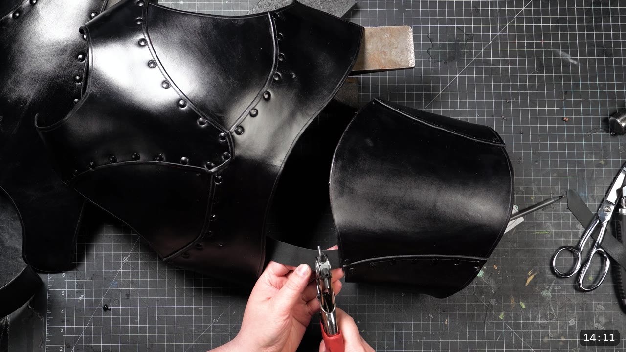 punching a hole in a black buckle strap with a rotary punch next to the dyed black breastplate panels