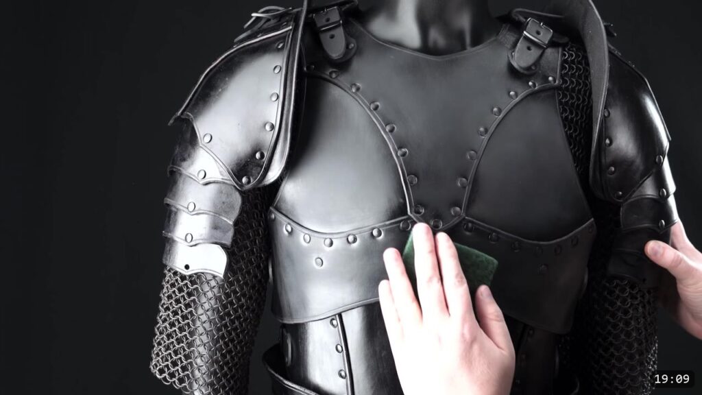 rubbing a green Scotch-Brite pad across the finished black breastplate worn on a mannequin with pauldrons and chainmail