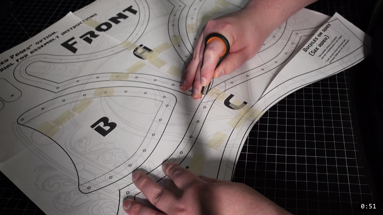 cutting out a printed Warrior breastplate pattern sheet labeled FRONT with lettered pieces B and C and a note reading buckles on sides