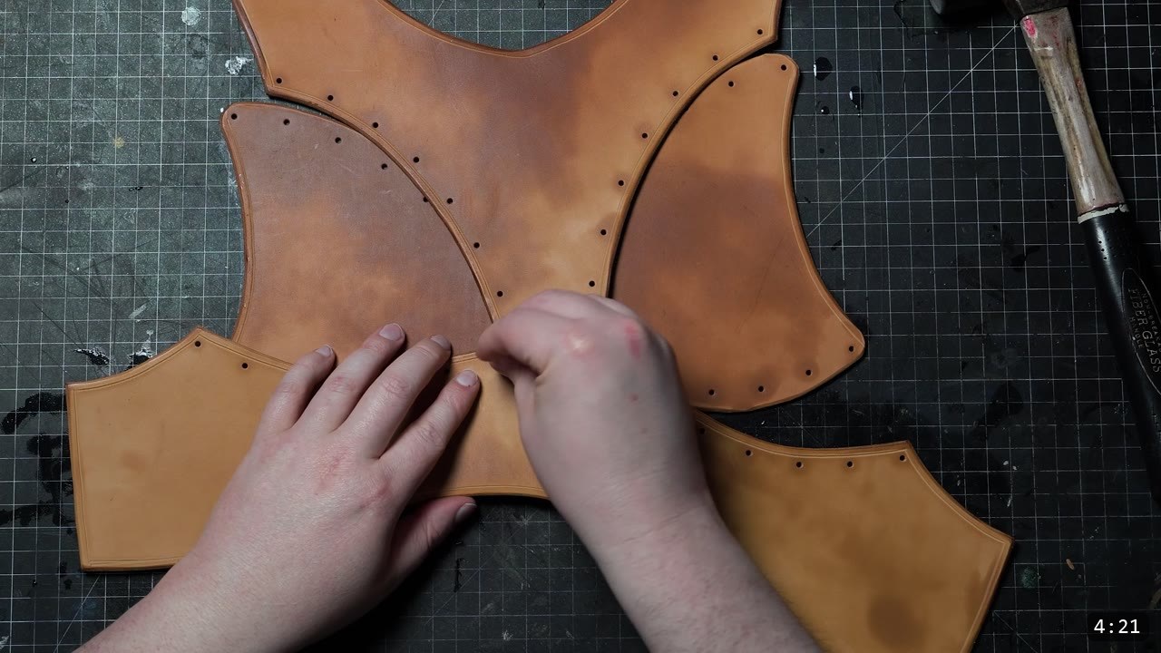 four cut tan breastplate panels arranged in a cross with punched rivet holes along the seams, hands aligning the center pieces