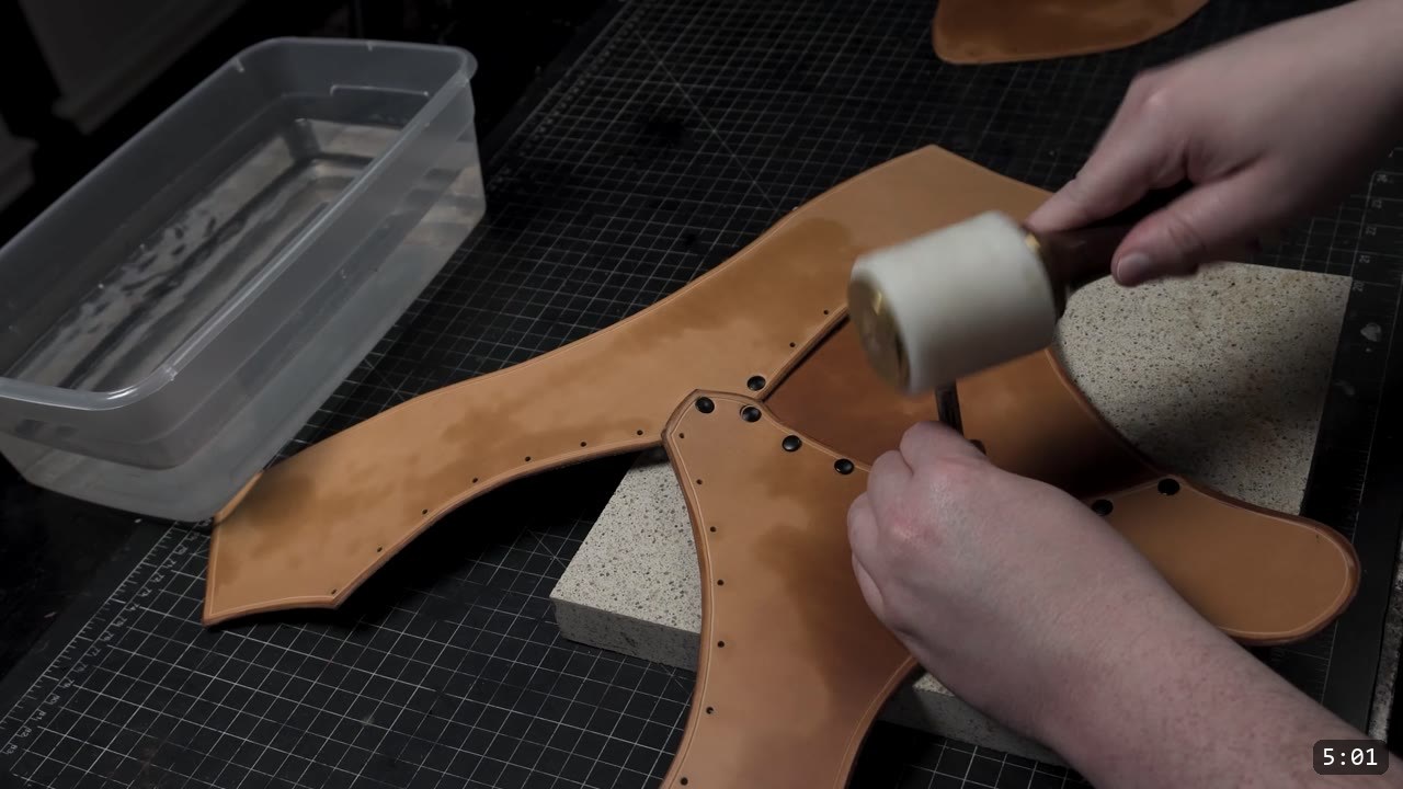 striking a rivet setter with a white mallet on the tan chest plate over a granite slab, a tub of water beside the bench