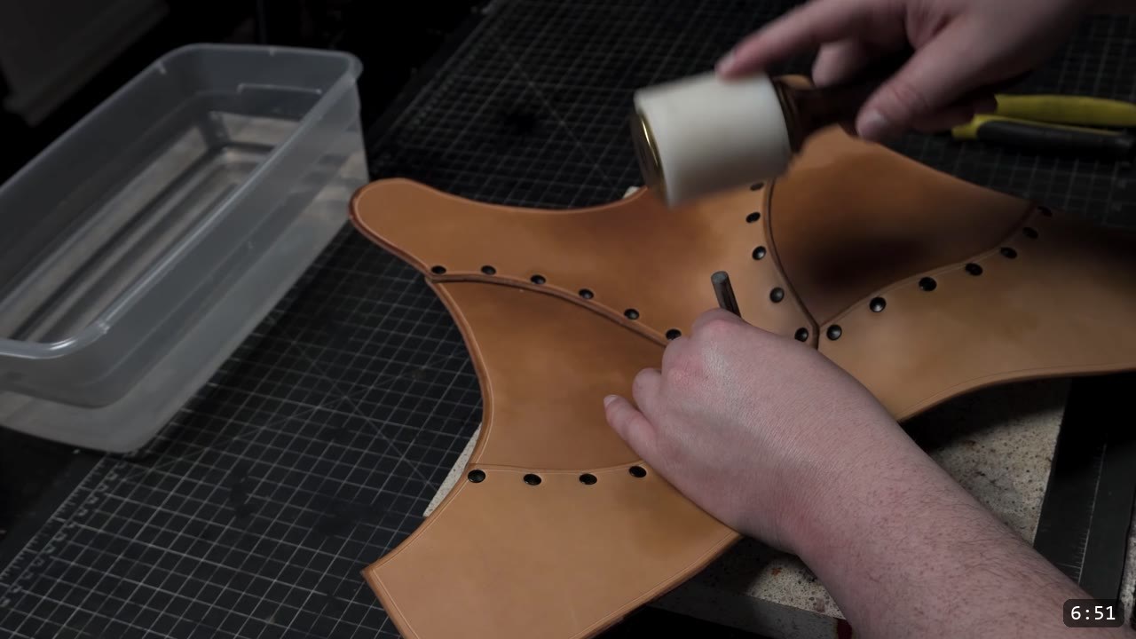setting rivets with a setter and mallet on the tan chest plate as the domed chest shape begins to form, water tub at the bench