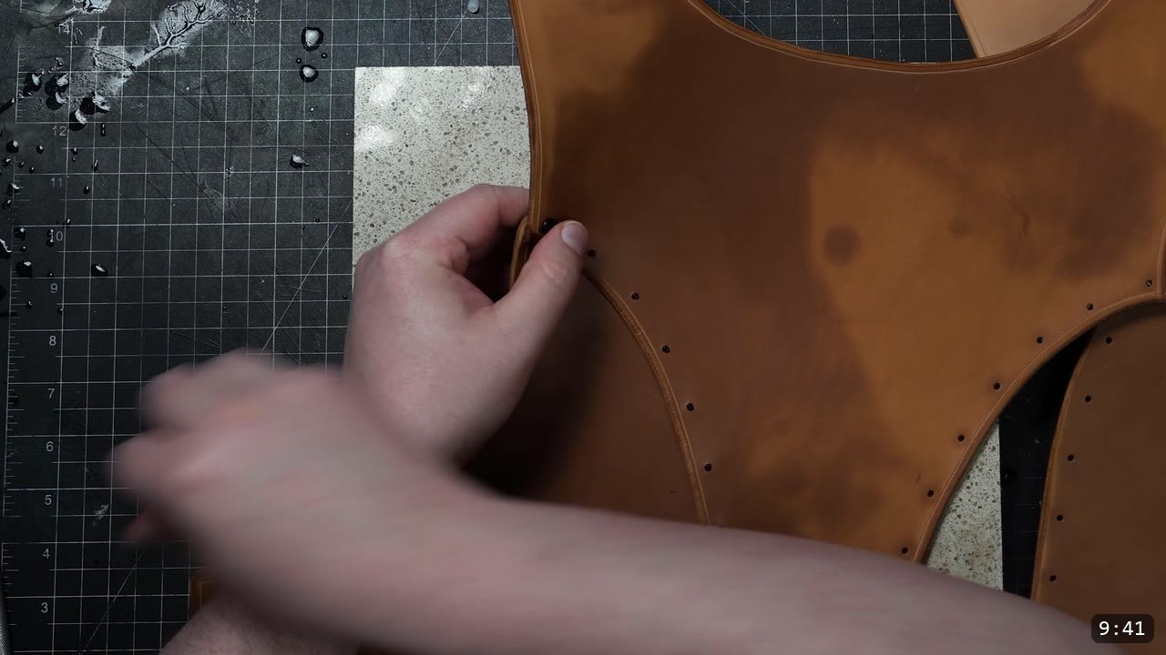 aligning a tan breastplate panel with punched rivet holes along the seam, on a granite slab with water droplets