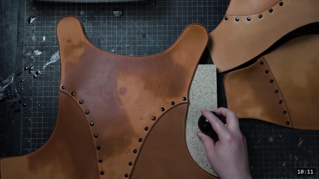 pressing a small black ball into a riveted tan plate against a granite block to dome it, other riveted plates laid out around it