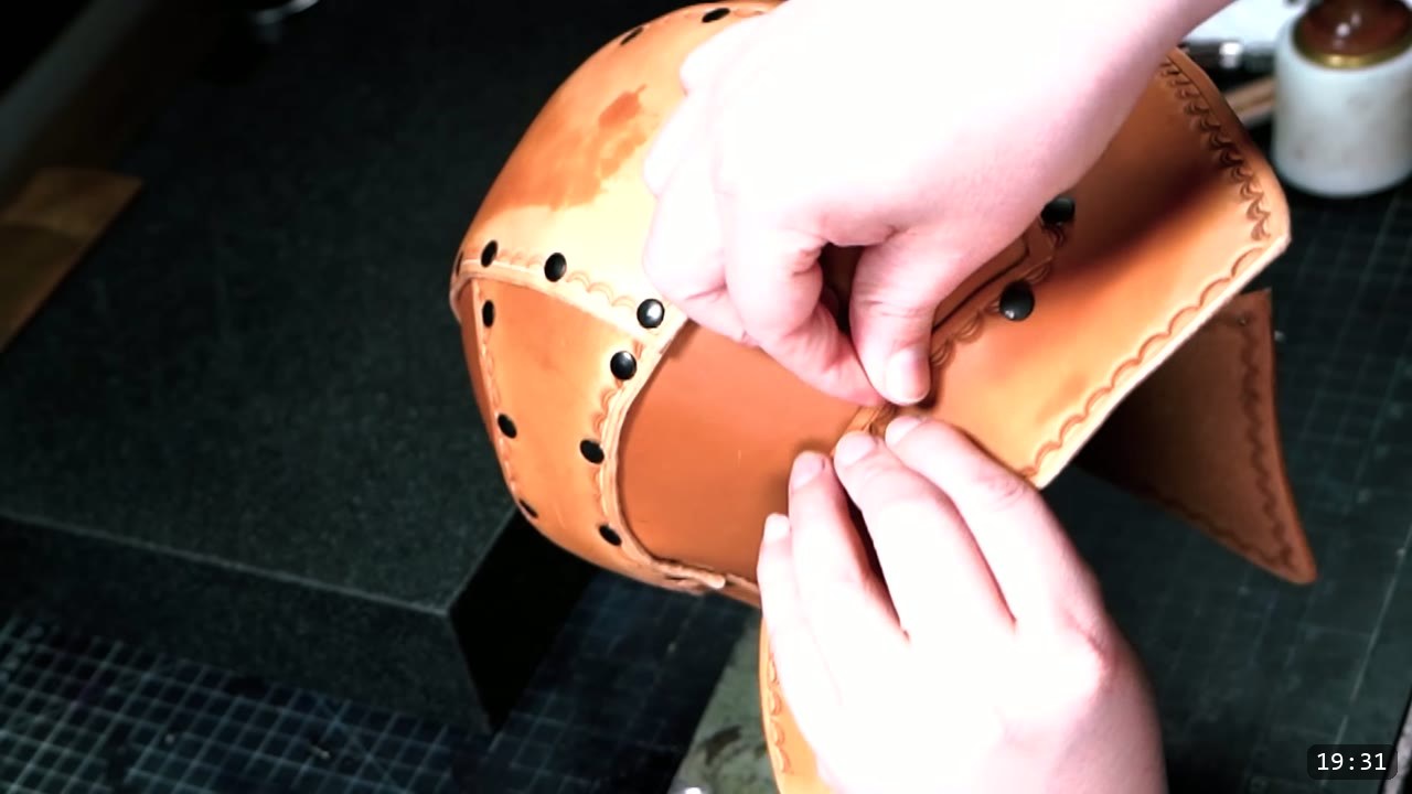 Leather Warrior Helmet Build Guide: Flat Pattern to Finished Piece 12 hands fitting the flared stamped tail piece against the riveted tan helmet dome, black rivets along the seams
