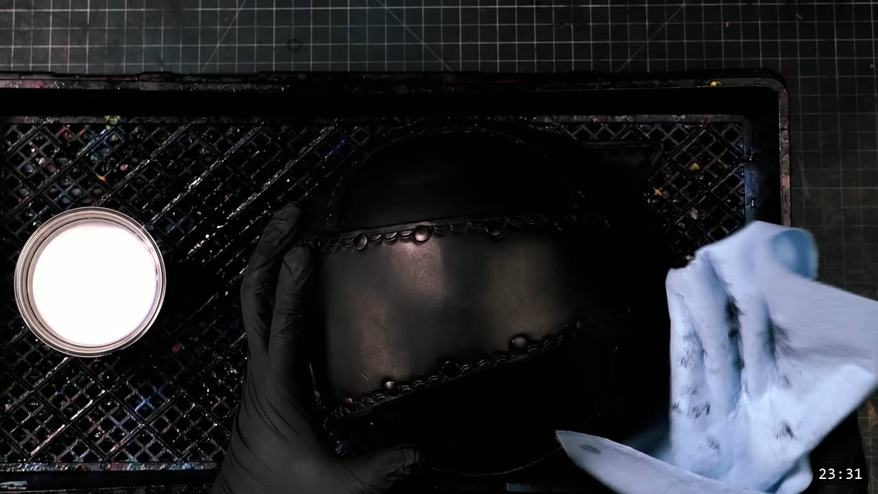 Leather Warrior Helmet Build Guide: Flat Pattern to Finished Piece 15 a black-gloved hand holding the dyed-black helmet over the dye rack, a tub of finish to the left, wiping the surface with a shop towel