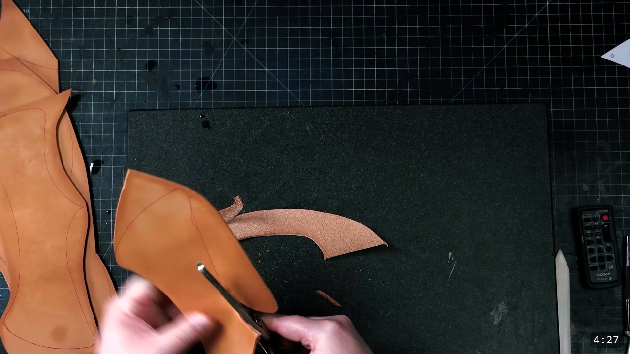Leather Warrior Helmet Build Guide: Flat Pattern to Finished Piece 4 hands trimming a curved tan leather piece with red traced guidelines against a hard black cutting board