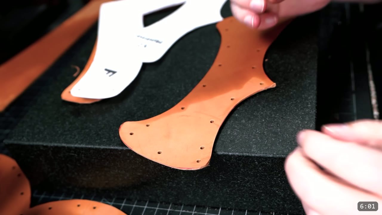 Leather Warrior Helmet Build Guide: Flat Pattern to Finished Piece 5 lifting the paper pattern off a cut tan side piece with rows of punched rivet holes along its edges