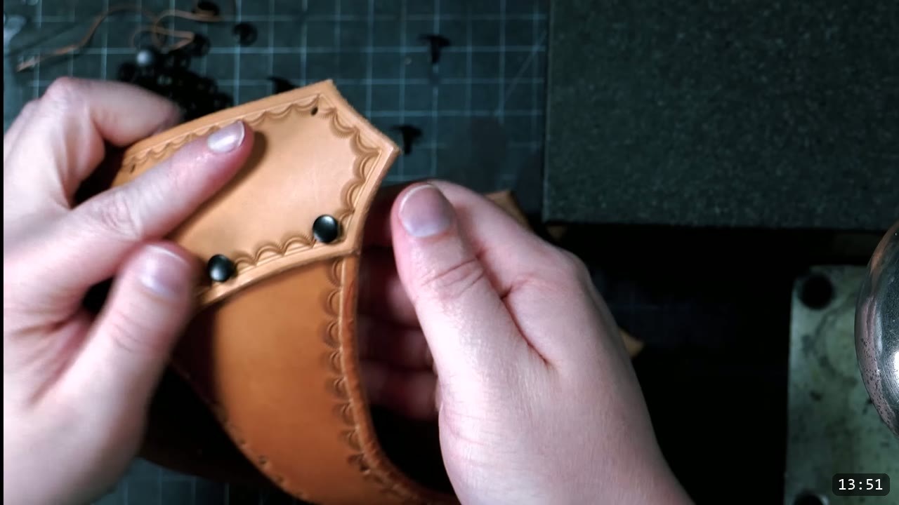 Leather Warrior Helmet Build Guide: Flat Pattern to Finished Piece 9 hands holding a crescent-stamped tan piece with two black double-cap rivets set into its edge
