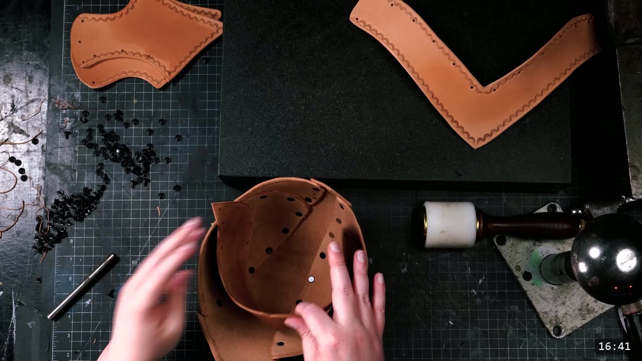Leather Warrior Helmet Build Guide: Flat Pattern to Finished Piece 10 a partly-riveted tan crown forming in the hands, loose rivets and a mallet nearby, stamped tail and cheek pieces at the top of the bench